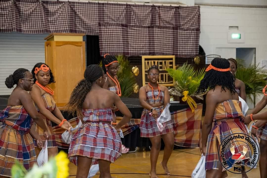 Young women in matching plaid wrappers performing a traditional Igbo dance on stage