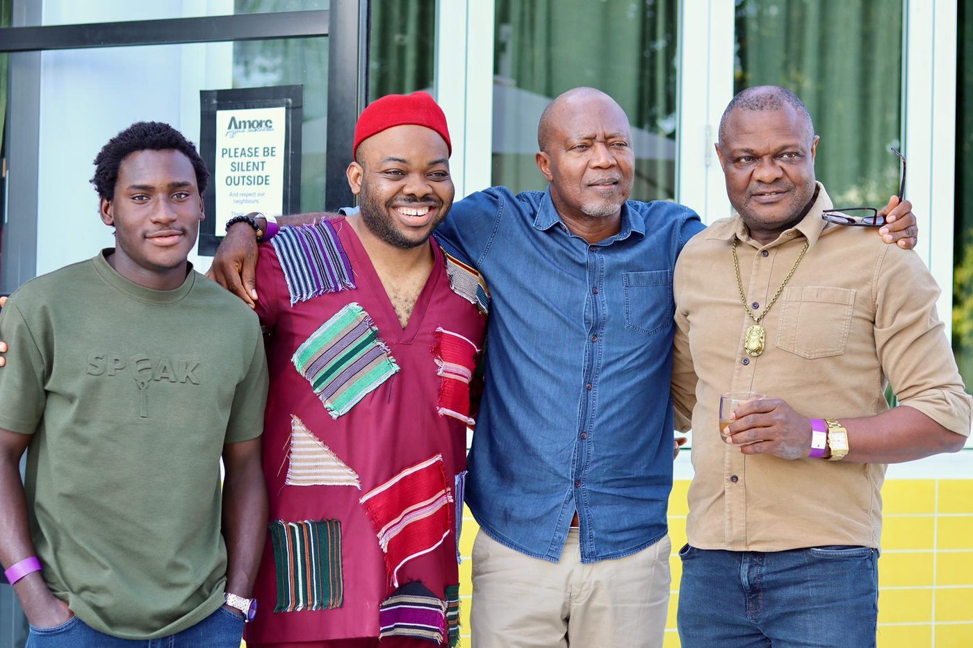 Four Nwannedinamba members smiling together, one wearing a red Igbo cap and isiagu-style top