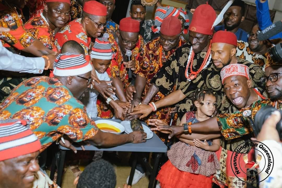 Nwannedinamba members in red caps and Ankara prints joining hands together in a circle